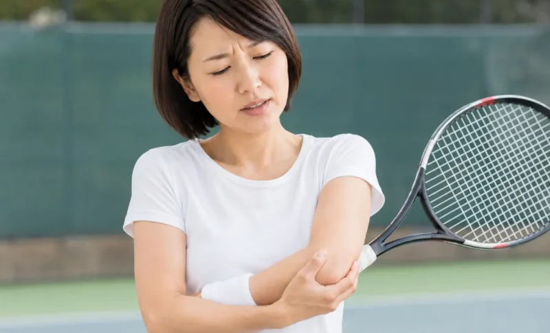 テニス中に肘の外側を押さえ、テニス肘による痛みに悩む女性