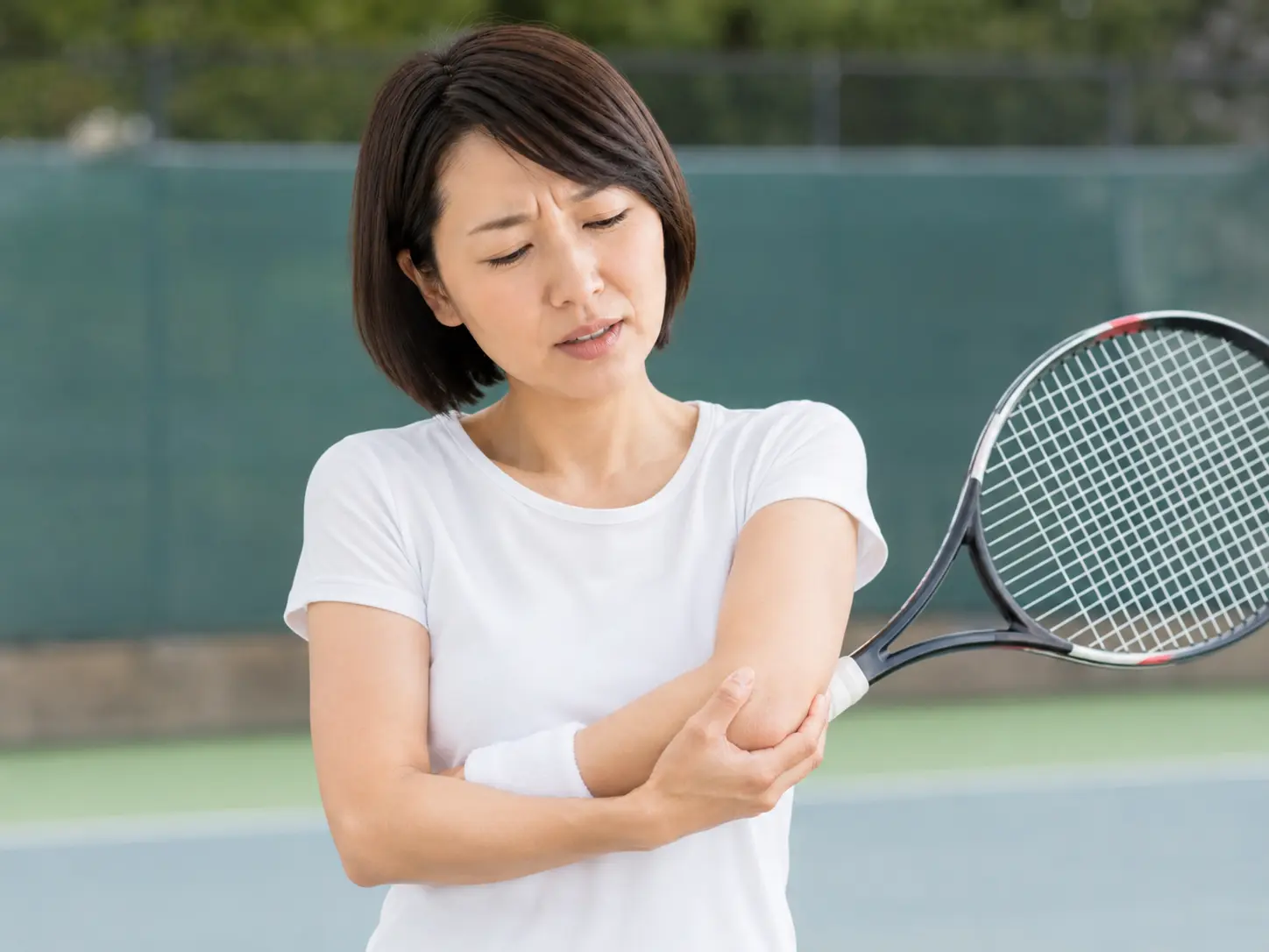 テニス中に肘の外側を押さえ、テニス肘による痛みに悩む女性