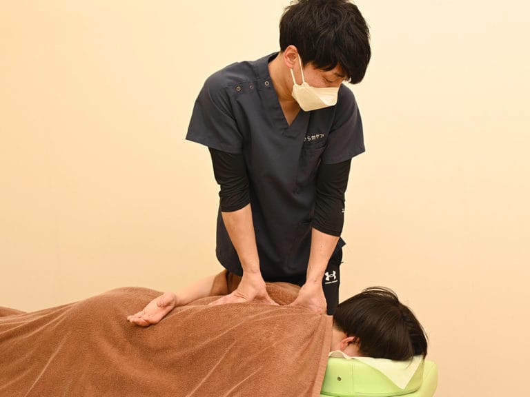 うつ伏せの方の背中に両手を当てて施術するスタッフ
