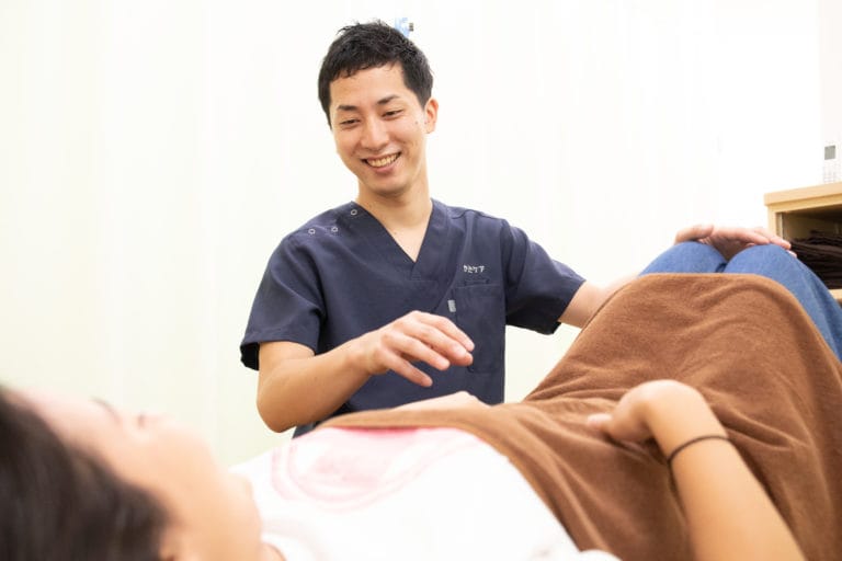 仰向けで膝を立てた方に、スタッフが声をかけながら身体を確認する様子 仰向けで膝を立てた方に、スタッフが声をかけながら身体を確認する様子