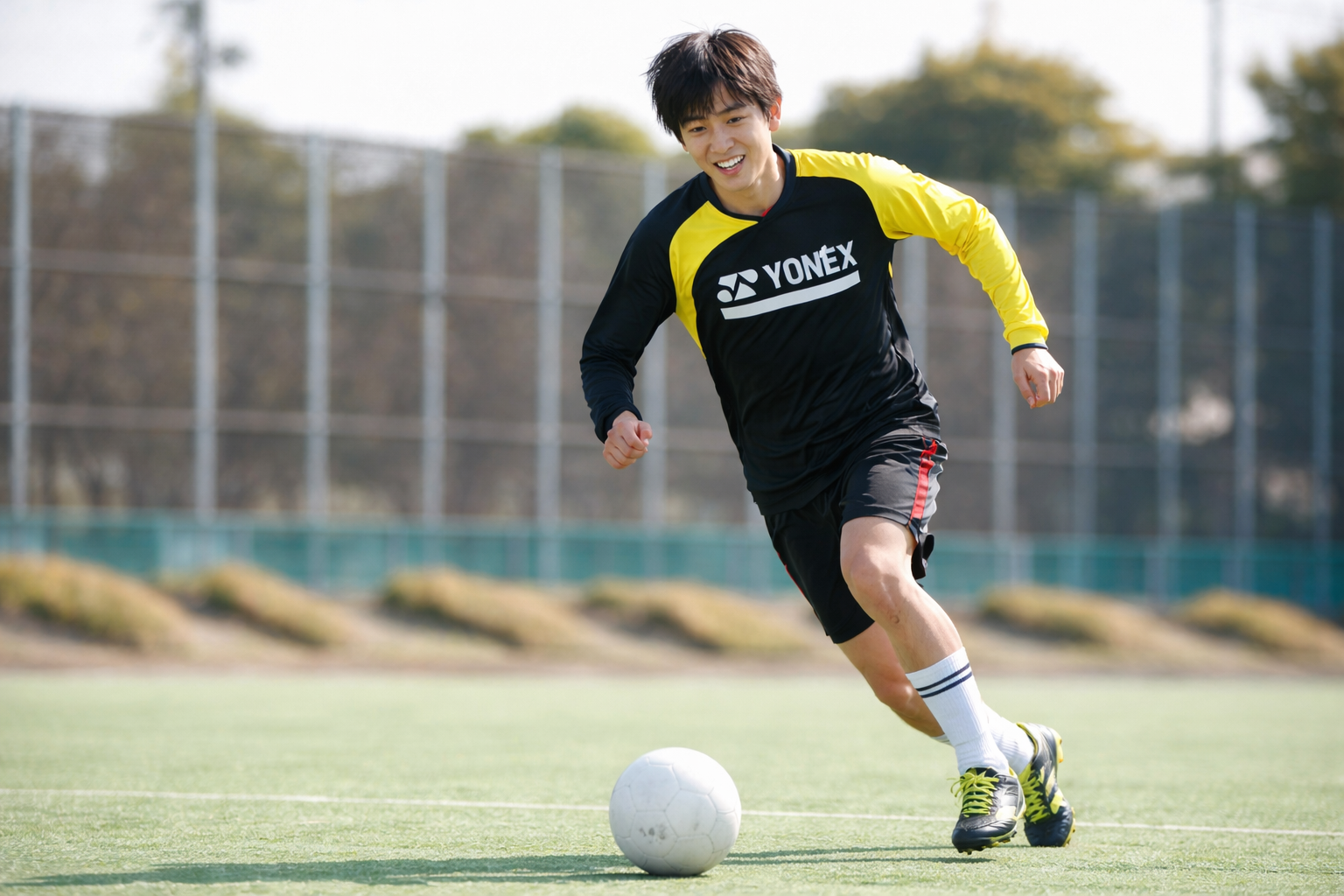 「サッカーの練習中に笑顔でボールを追いかけて走る男子選手。痛みのない状態で元気にプレーしている様子」