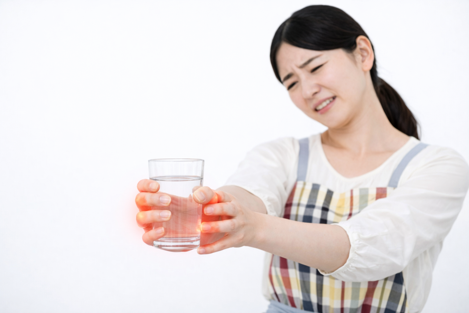 「コップを持つ手に痛みを感じ、つらそうな表情を浮かべる女性。指先や手首のしびれ・痛みの様子を示したイメージ。」