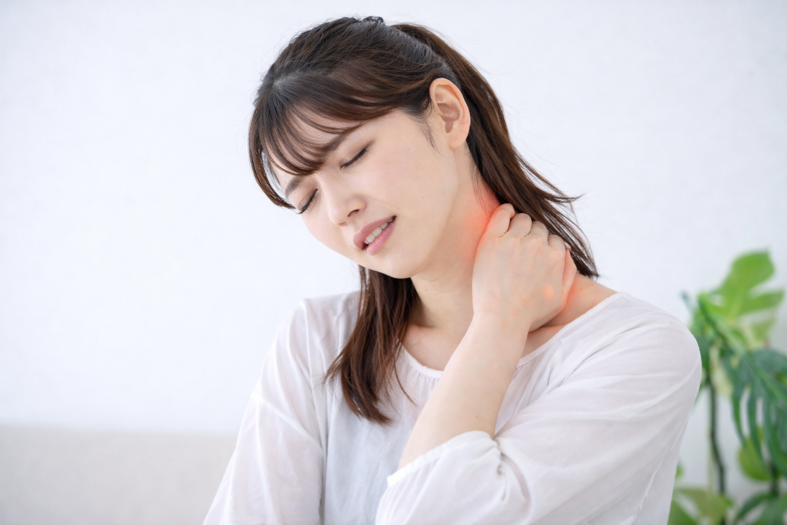 「首の痛みに顔をゆがめ、つらそうに首の後ろを押さえる女性。頸椎の不調や肩こり、神経圧迫による痛みを示すイメージ。」