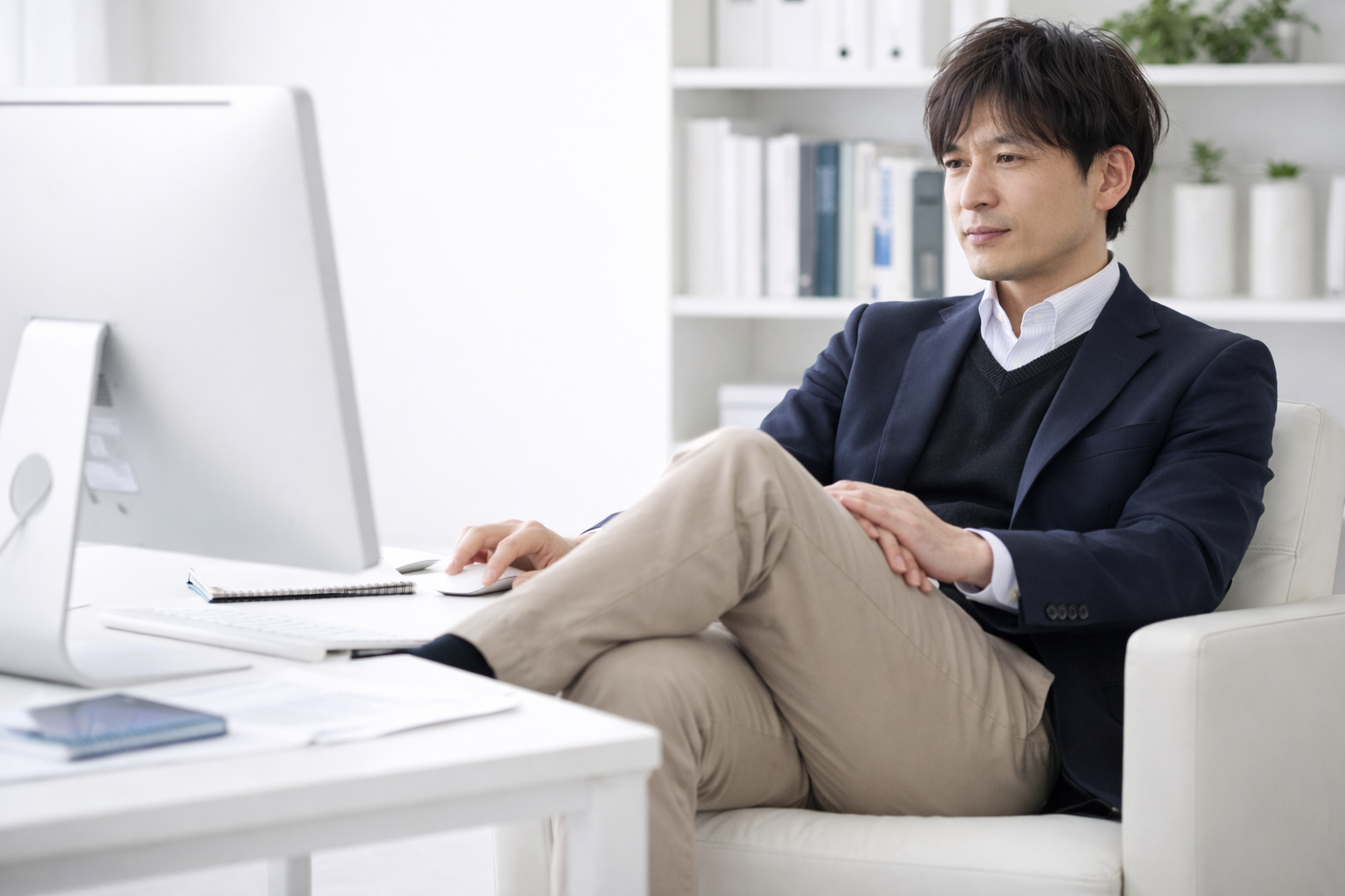 オフィスでデスクワーク中の男性が、足を組んでパソコン画面を見つめている様子。