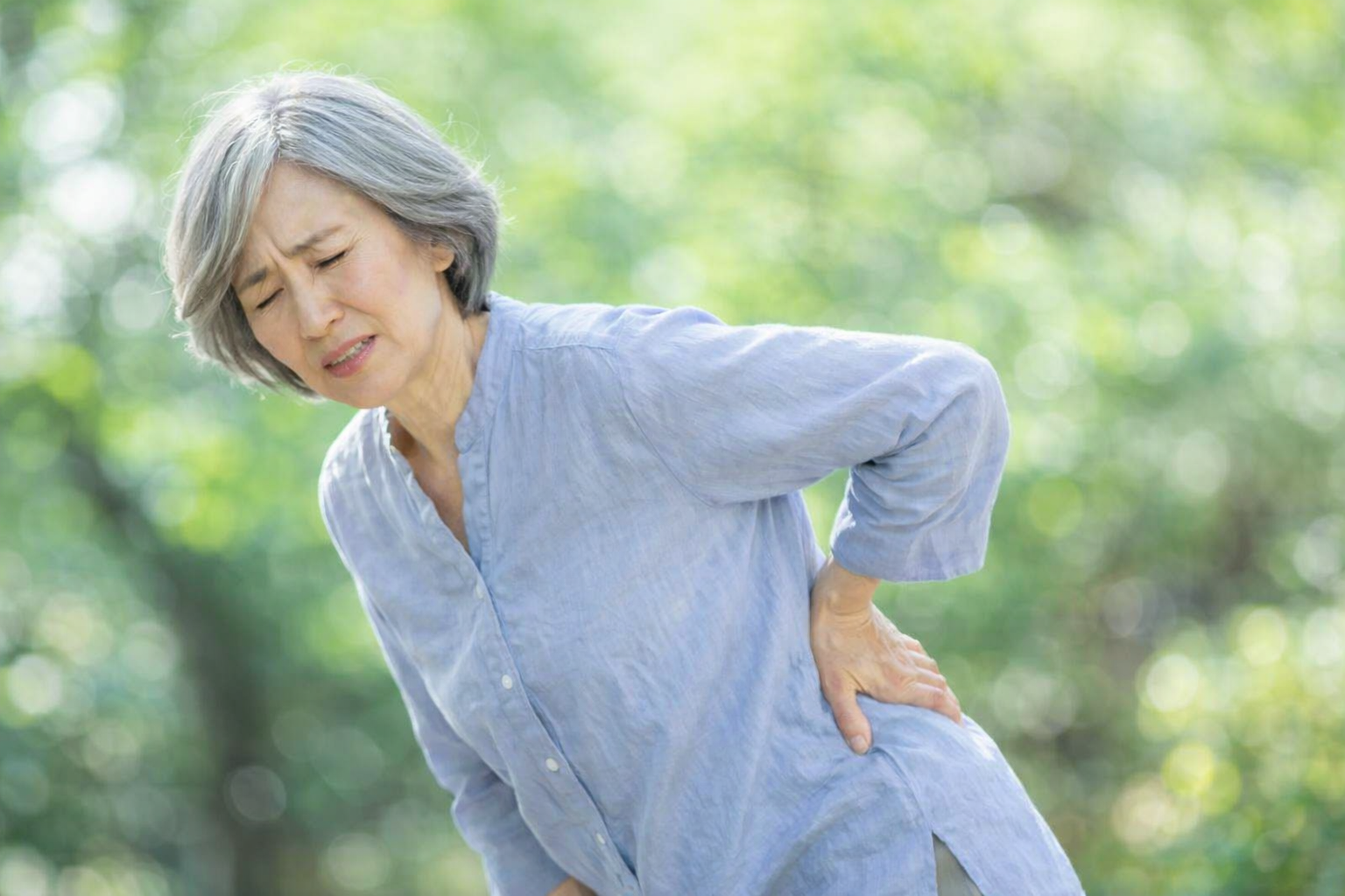腰の痛みに顔をしかめ、手を当てて支える高齢女性。圧迫骨折による腰痛のつらさを表現したイメージ。 