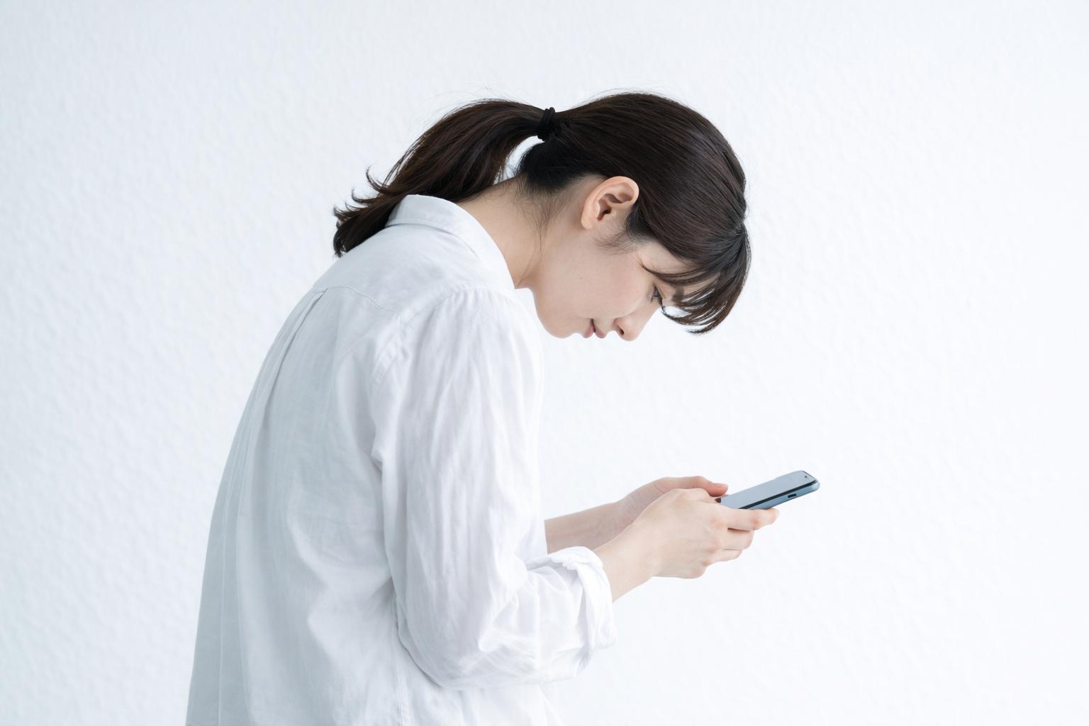 スマートフォンを見て前かがみになっている女性。猫背・姿勢不良のイメージ