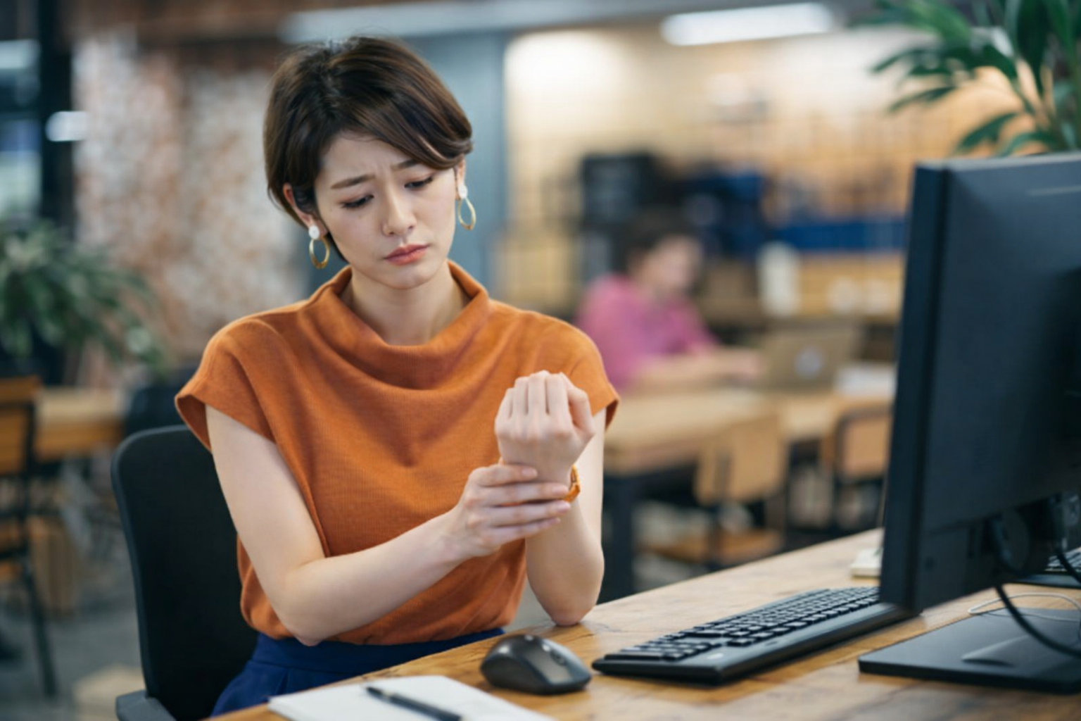 パソコン作業中に手首の痛みを感じ、不安そうな表情で手首を押さえる女性。手関節インピンジメントの症状を示すシーン。 