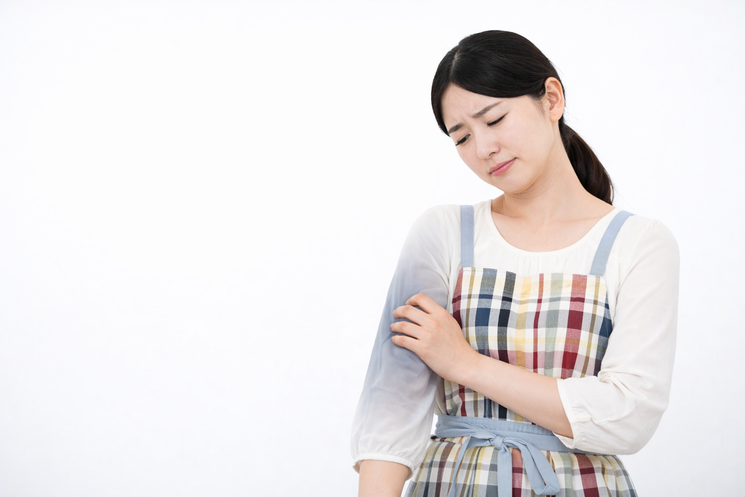 「腕の痛みを感じ、不快そうに二の腕を押さえるエプロン姿の女性。家事中の疲労や神経・筋肉の不調を訴えている様子。」