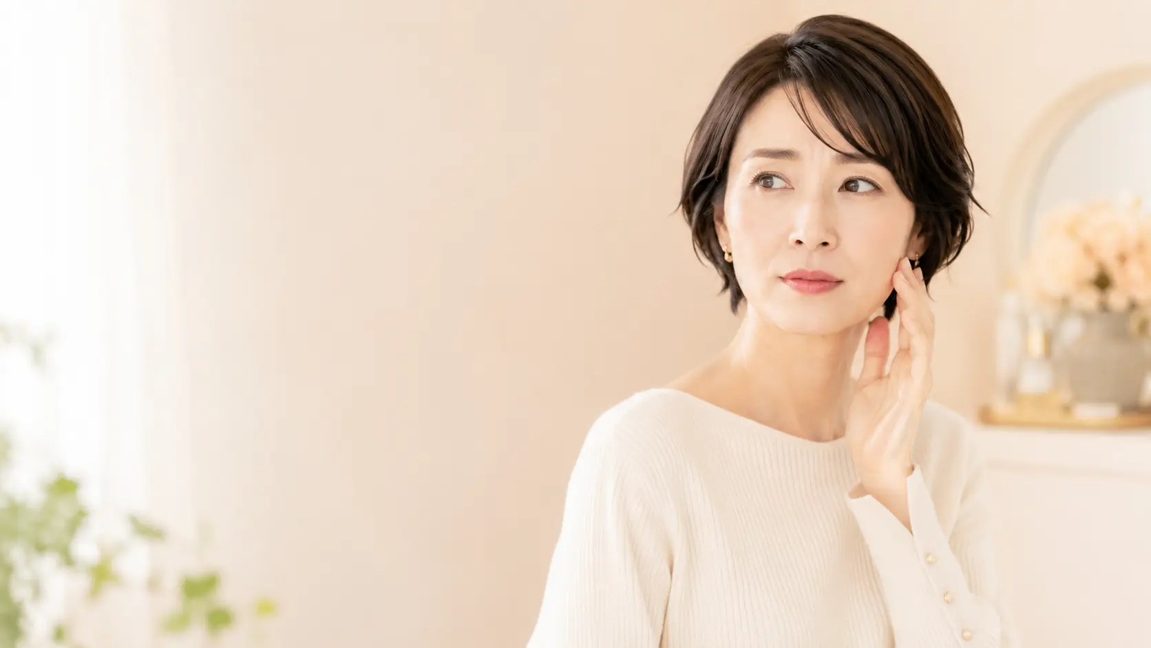 美容鍼の効果や仕組みに関心があり、顔に手を添えて肌やフェイスラインの変化を確認する女性。