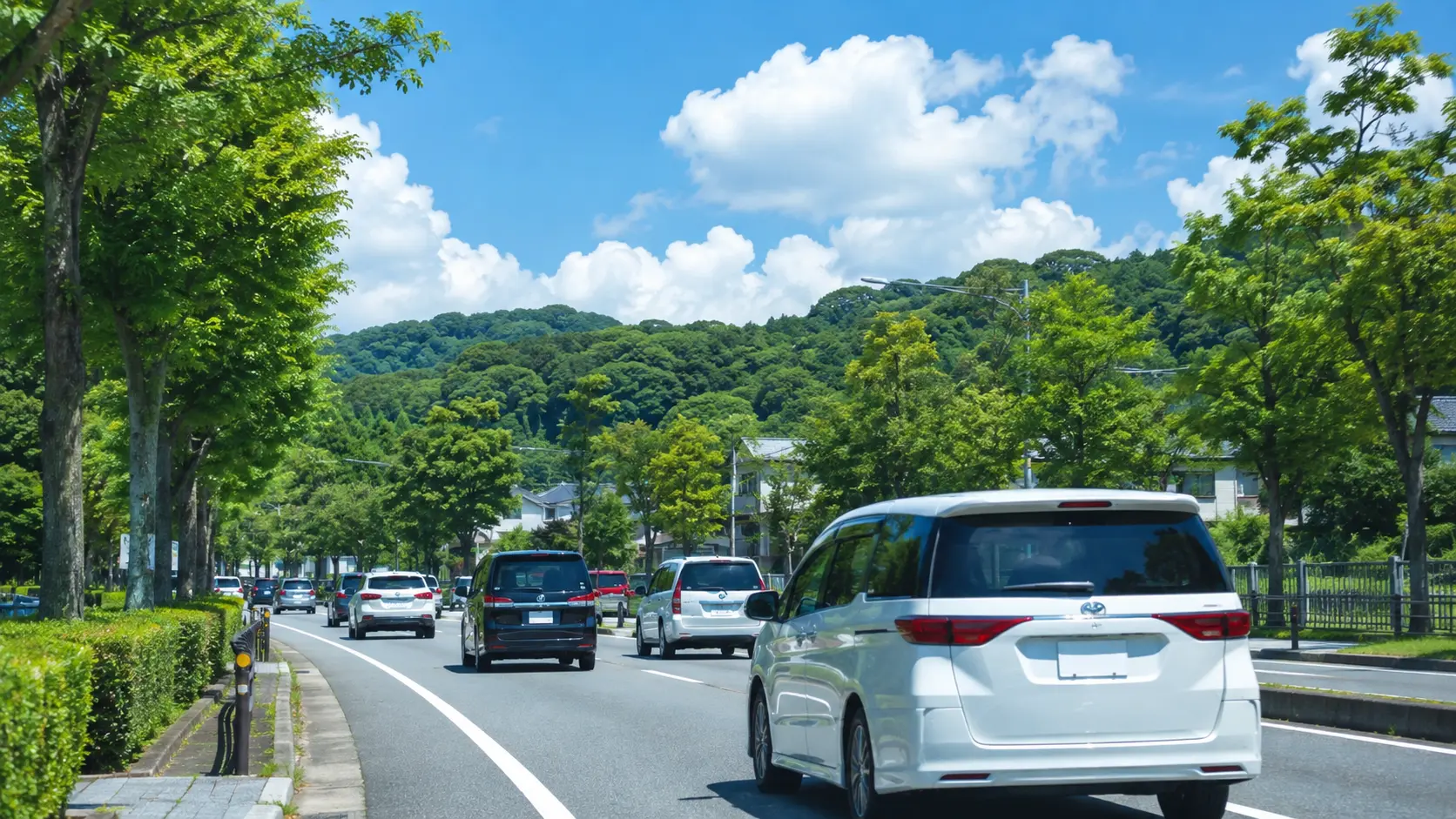 青空と緑に囲まれた道路を多くの車が走る、お盆の帰省・外出シーズンのイメージ