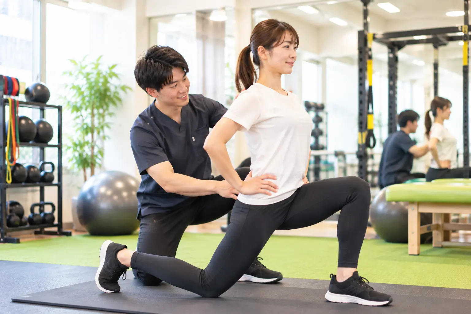 からだケア整骨院で、スタッフのサポートを受けながら姿勢や身体の使い方を意識したトレーニングを行う日本人女性