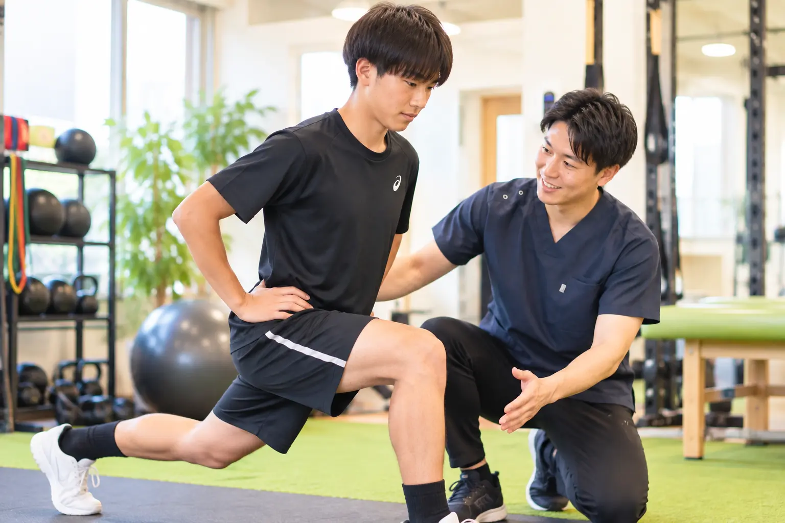 からだケア整骨院で、スタッフのサポートを受けながらスポーツによる痛みの改善と競技復帰に向けた下半身トレーニングを行う日本人男性