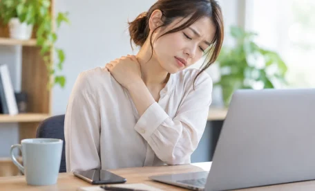 スマホやパソコン作業のあとに首・肩の重さを感じ、肩を押さえる女性｜デスクワークによる首肩の負担