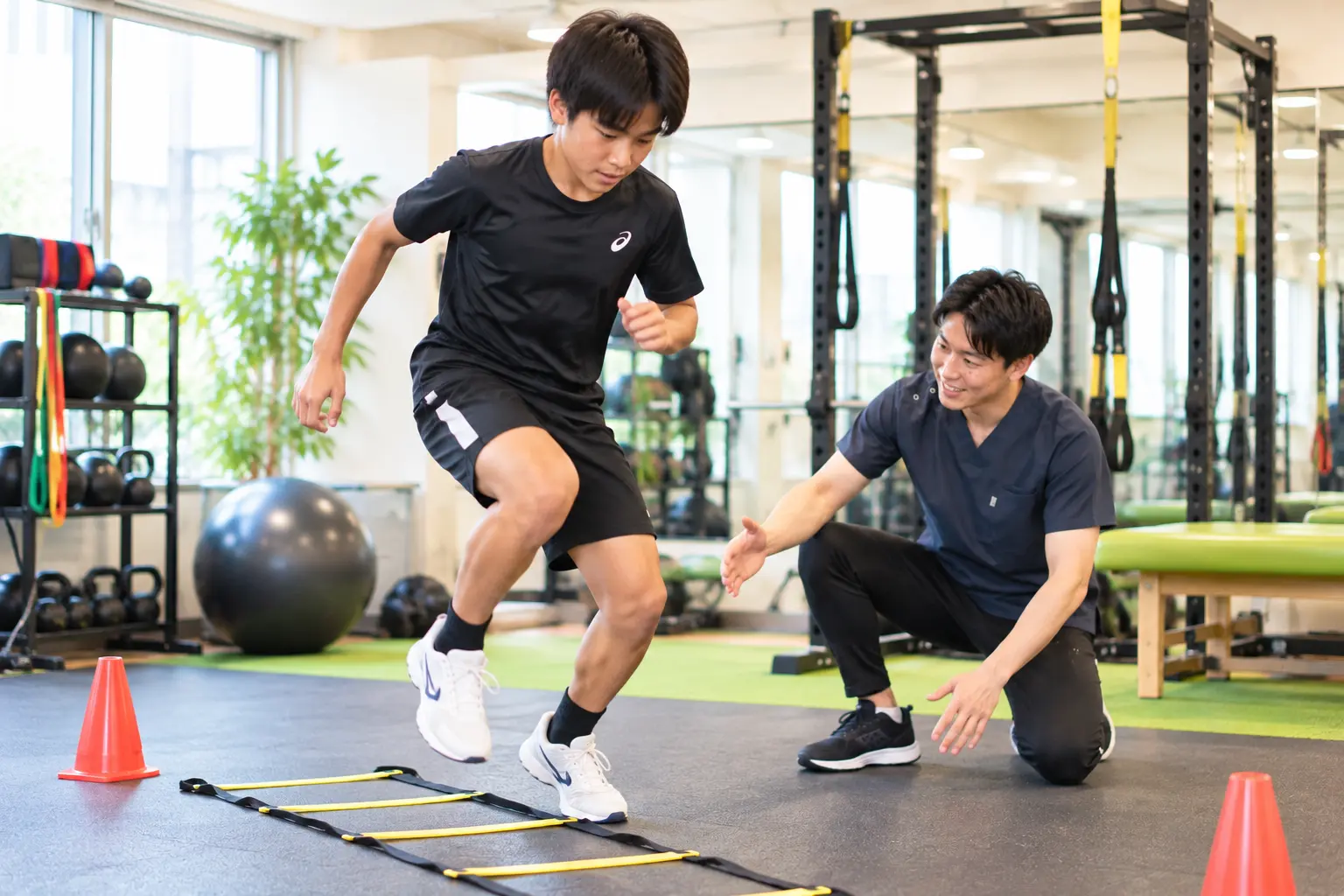 からだケア整骨院で、スタッフのサポートを受けながらラダーを使ったスポーツパフォーマンス向上トレーニングを行う日本人男性