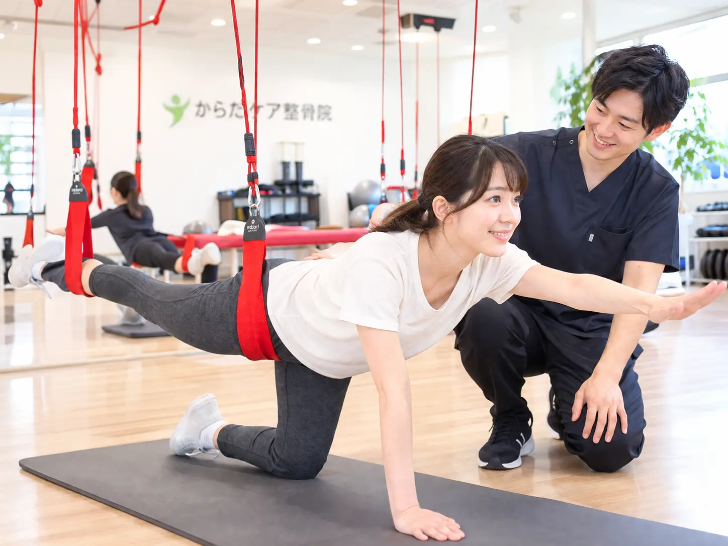日野本院でレッドコードを使い、スタッフのサポートを受けながら体幹・バランストレーニングを行う女性の様子。