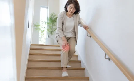 階段を降りる際に膝の痛みを感じ、膝を押さえる女性｜階段下降時の膝痛