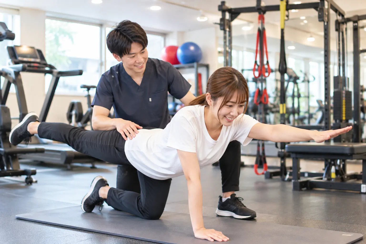 からだケア整骨院 日野本院のトレーニング施設で、スタッフのサポートを受けながら体幹トレーニングを行う日本人女性