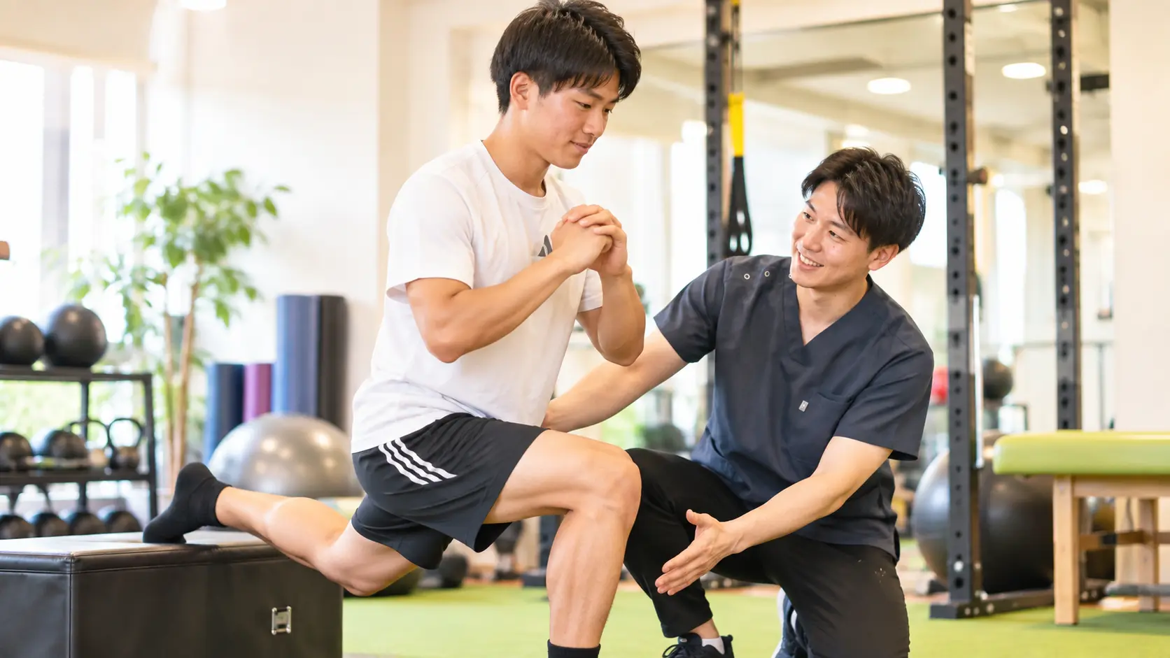 からだケア整骨院で、スタッフのサポートを受けながらケガ後の運動・競技復帰に向けた下半身トレーニングを行う日本人男性