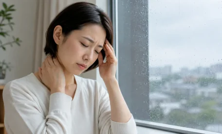 雨の日に頭痛と首の重さを感じ、こめかみと首を押さえる女性｜気圧・天候変化による不調